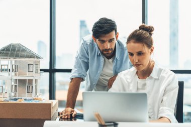 Genç yetenekli proje yöneticisi, modern ofis veya mimarlık stüdyosundaki proje planını kullanarak, Kafkas mühendisi ev modunu incelerken dizüstü bilgisayar kullanarak çalışıyor. İnşaat mühendisliği, yaratıcı tasarım. İzleme.