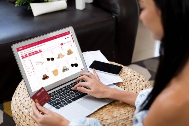 Genç bir kadın dizüstü bilgisayarla ürün sipariş eder ya da satın alır ve akıllı telefondan işlem ödemesi yapar. İnternet bankacılığı vasıtasıyla internet üzerinden kredi kartıyla online alışveriş hayatı. Blithe