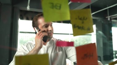 Profesyonel işadamı renkli yapışkan notlara yazılmış pazarlama stratejisi fikrine bakarken müşterilerine telefon ediyor. Proje yöneticisi duvardaki telefon analiz verileriyle konuşuyor. Yönlendirici.
