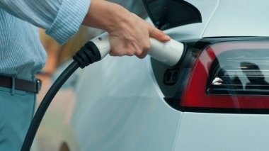 Yolculuk sırasında doğal orman ya da milli parktaki elektrikli araba için şarj olan genç bir kadın. Tatil ve tatil boyunca çevre dostu seyahat. Yükselt