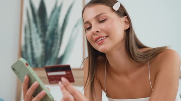オンライン決済アプリとスマートフォンのデジタルウォレットを使用してベッドに横たわる若い女性は クレジットカードで支払う モバイルインターネットを介して商業ショッピングとモダンな購入 アディット — ストック動画
