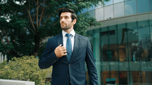 Handsome caucasian business man standing in front of building. Skilled investor looking around while pose cool at camera. Smart project manager wearing formal suit. Vision and professional. Exultant.