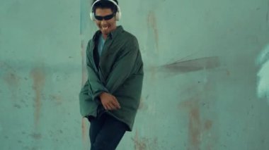 Hippi, şehir caddesinde hip-hop dinlerken kulaklık takıyor. Sokak dansçısı ayak seslerini kulaklıktan müziğe taşıyor. Açık hava sporu 2024. Çimento arka planı. Moda. Aktif stil. hiphop.
