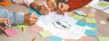 Profesyonel başlangıç grubu zihin haritası kullanarak yaratıcı pazarlama fikrini paylaşıyor. Genç yetenekli iş adamları yapışkan notlar yazarken beyin fırtınası planı yapıyorlar. Eline odaklan. - Yakın çekim. Değiştirilmiş.