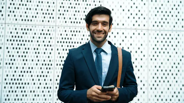 Portrait image of successful young business man looking at camera while hold phone with white background. Attractive caucasian investor or project manager standing at building. Close up. Exultant.