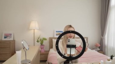 Sosyal medya için güzellik ve kozmetik video içeriği hazırlayan genç bir kadın. Güzellik blogcusu kamera ve ışık halkası kullanarak seyirciye ve takipçiye nasıl göz farı uygulanacağını gösteriyor. Blithe