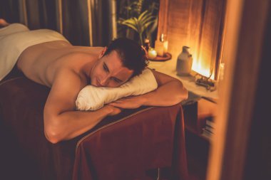 Beyaz erkek müşteri stres önleyici spa masajının keyfini çıkarıyor ve lüks otel ya da oteldeki ortam kaplıcalarında sıcak mum ışığında güzellik teniyle eğleniyor. Sessiz.