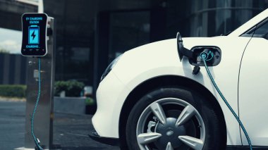 Şehir merkezinin otoparkındaki şarj istasyonuna bağlı elektrikli araba. Alternatif temiz ve sürdürülebilir enerji kullanan geleceğin yenilikçi yenilenebilir EV arabası. İnceleyin