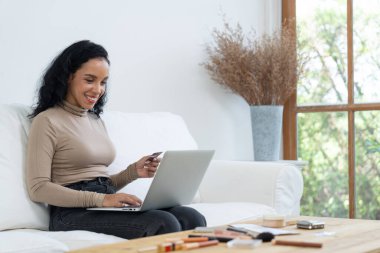 Genç mutlu bir kadın internetten alışveriş yaparak ürün satın alırken aynı zamanda internet üzerinden online kredi kartı ödeme sistemi ile çevrimiçi mağaza platformundan önemli siber güvenlik tarafından korunan ürünler sipariş ediyor.