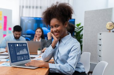 Bir grup ofis çalışanı ile birlikte arka planda ekranda gösterim paneliyle buluşan mutlu Afrikalı genç bir iş kadını portresi. Takım toplantısında kendine güveni tam bir ofis hanımı. Uyum