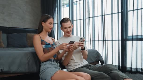 若いカップルは クレジットカードで支払うためにスマートフォンでオンライン決済アプリとデジタルウォレットを使用してホームベッドルームに座っています モバイルインターネットを介して商業ショッピングとモダンな購入 アディット — ストック動画