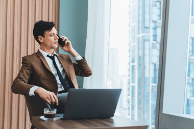 Gökdelen manzaralı pencerenin yanında otururken yakışıklı iş adamının müdürle telefon görüşmesi yaptığı yakın plan. Yönetici, telefon ve dizüstü bilgisayarla konuşuyor. Önüne bak. Süslü.