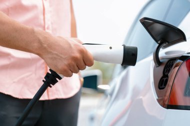 Dışarıdaki şarj istasyonundan EV şarj aletini şarj etmek için elektrikli araca elle tak. Alternatif temiz ve sürdürülebilir enerji kavramına sahip taze gün ışığı ortamı. Kalıcı