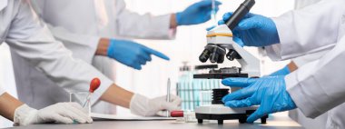 Kendini adamış bir grup bilim adamı yeni bir aşı ilacı ya da antibiyotik geliştirmek için tıbbi laboratuvarda mikroskop kullanarak kimyasal deney yapıyorlar. Biyoteknoloji laboratuvarı ve tıp araştırma konsepti. Neoterik