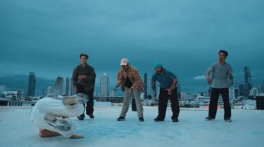 Profesyonel hippi hareketsiz poz verirken aynı zamanda şehir manzaralı çatıdaki müziğe ayak basıyor. Break dansçı, hip-hop dansçıları grubuyla birlikte sokak dansı yapıyor. Açık hava sporu 2024 hiphop..