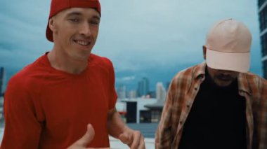 Çok kültürlü veya çok kültürlü hipster grupları şık ve renkli giysiler giyerek çatıda şehir manzaralı ve gökyüzü kazıyıcılarıyla dans ederler. Canlı sokak dansı konsepti. Açık hava sporu 2024 hiphop..