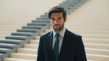 Akıllı iş adamı merdivenlerde kameraya bakıyor. İş elbisesi giyerken kameraya gülümseyen başarılı adamın yakın çekimi. Yönetici, kameraya bak. Hareket eden kamera. Sevinçli..