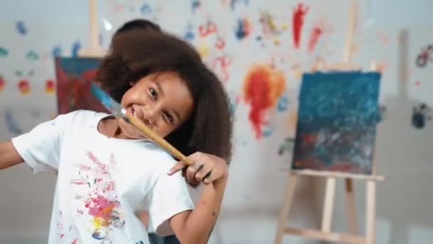 キュートなアフリカの少女は 学生が後ろにキャンバスを描いている間 ブラシを保持しています 多文化の子供たちがアートレッスンに出席し カメラを見ながら学習する クリエイティブ活動コンセプト エラー — ストック動画
