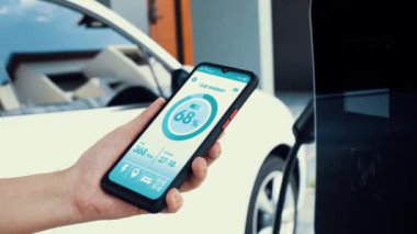 Akıllı telefon ekranı akıllı EV mobil uygulama üzerinde pil durumu EV araba garajdaki ev şarj istasyonu ile elektrik şarj ederken. Geleceğin yenilikçi EV arabası ve enerji sürdürülebilirliği. İnceleyin