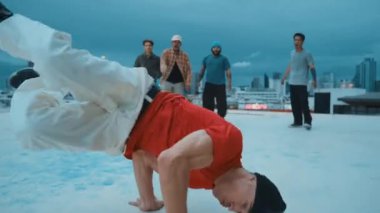 Profesyonel hippi hareketsiz poz verirken aynı zamanda şehir manzaralı çatıdaki müziğe ayak basıyor. Break dansçı, hip-hop dansçıları grubuyla birlikte sokak dansı yapıyor. Açık hava sporu 2024 hiphop..