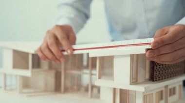 Profesyonel erkek mimar ev modelinin uzunluğunu ölçmek için cetvel kullanırken, beyaz tenli genç meslektaşı ev modeliyle toplantı masasındaki verileri analiz etmek için dizüstü bilgisayar kullanıyor. Tertemiz..