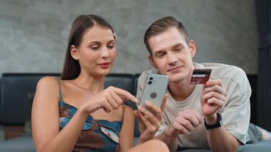 Genç çift, kredi kartıyla ödemek için internet üzerinden ödeme uygulaması ve dijital cüzdan kullanarak yatak odasında oturuyor. Mobil internet üzerinden alışveriş ve modern alımlar. Düzenle