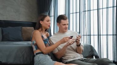 Genç çift, kredi kartıyla ödemek için internet üzerinden ödeme uygulaması ve dijital cüzdan kullanarak yatak odasında oturuyor. Mobil internet üzerinden alışveriş ve modern alımlar. Düzenle