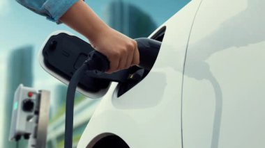 Adam elektrikli arabaya akıllı EV şarj cihazı takıyor ve arka planda modern şehir manzarası olan EV şarj istasyonundan şarj oluyor. ESG şehrinde gelecekteki sürdürülebilir güç ve EV araba kullanımı. İnceleyin