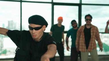 Profesyonel hipster, çeşitli çok kültürlü arkadaşlarıyla birlikte adım atıp dans ediyor. Gökyüzü dövüşçüsü ve şehir manzaralı pencerenin yanında duruyor. Break dans. Açık hava sporları konsepti 2024 hiphop..