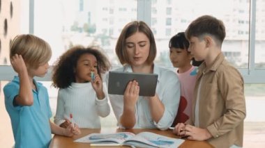 Bir grup öğrenciye çevrimiçi ders verirken elinde tablet tutan akıllı öğretmen. Yetenekli eğitmen mühendislik derslerini anlatırken genç öğrenci oturuyor ve sunumu dinliyor. Etkinlik.