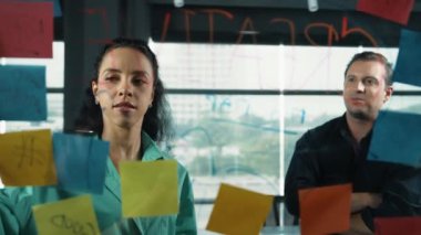 Profesyonel iş adamları yaratıcı pazarlama fikrini modern ofiste tartışırlar. İş adamları cam tahtada yapışkan notlar kullanarak finansal plan üzerinde çalışıyor. Yönlendirici.