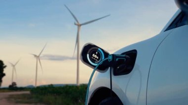 Elektrikli araba, EV şarj istasyonundan enerji alıyor. Rüzgar türbini çiftliğinde EV şarj kablosu kablosunun fütüristik akıllı batarya durum hologramını gösteriyor. Alternatif temiz enerji sürdürülebilirliği. İnceleyin