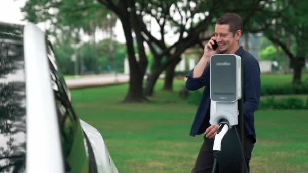 Seorang Pria Berbicara Telepon Sambil Mengisi Baterai Untuk Mobil Listrik — Stok Video