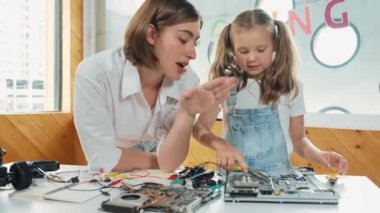 Genç, zeki, beyaz bir öğretmen öğrencilere elektronik kurulun bir parçasını öğretiyor. Uzman kız dijital elektrikli aletleri öğreniyor ve cips ve kablolarla ana kartı tamir ediyor. Etkinlik.