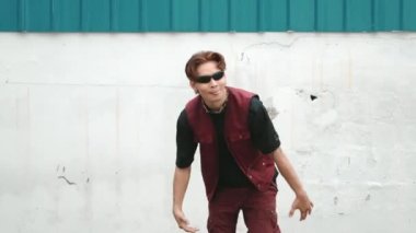 Beyaz arka planda break dans pratiği yapan yakışıklı bir sokak dansçısı. Hip hop tarzı giyinen sporcu, mavi arka planlı bir sokakta müzik eşliğinde ayak sesleri çıkarıyor. Açık hava sporu 2024 hiphop..