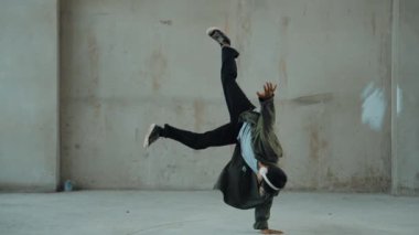 Hippi, şehir caddesinde hip-hop dinlerken kulaklık takıyor. Sokak dansçısı ayak seslerini kulaklıktan müziğe taşıyor. Açık hava sporu 2024. Çimento arka planı. Moda. Aktif stil. hiphop.