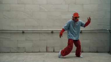 Yakışıklı koreograf gri arka planda sokak dansı yapıyor. Genç çekici erkek dansçı şık kıyafetler giyerken gösteri yapıyor. Hareketli bir adım. Uzayı kopyala Açık hava sporu 2024. Yumuşak bir şekilde..
