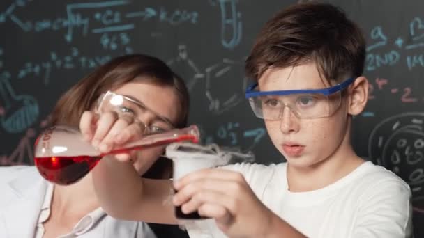 Zbliżenie Kaukaskiego Chłopca Mieszającego Płyn Chemiczny Podczas Gdy Nauczyciel Doradza — Wideo stockowe