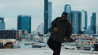Profesyonel hipster çatıda gökyüzü avcısıyla ya da şehir siteleriyle break dans yapıyor. Sokak dansı performansı için yetenekli Asyalı hip-hop dansçısı. Modern dans. Açık hava sporu 2024 hiphop..