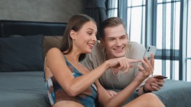Genç çift, online ödeme uygulaması ve dijital cüzdanı kullanarak kredi kartıyla ödeme yaptıktan sonra mutlu ve heyecanlı hissediyorlar. Mobil internet üzerinden alışveriş ve modern alımlar. Düzenle
