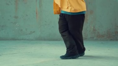 Profesyonel hipster sokak, şehir merkezinde ayak sesleri gösteriyor ya da pratik yapıyor. Genç break dansçı hareket ediyor ve kolunu ve bacağını esnetiyor. Açık hava sporu 2024. Gri arka plan. Hip hop modası. hiphop.