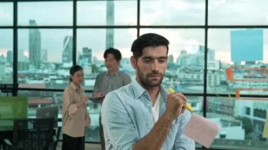 Profesyonel işadamı cam duvardaki yapışkan notları alıp üzerine yazarken Asyalı proje yöneticisi de gökdelen, şehir manzarasında projeye başlama konusunu tartışıyor, paylaşıyor, konuşuyor. İzleme