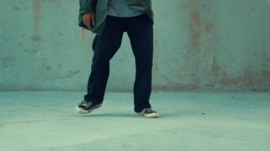Hippi, şehir caddesinde hip-hop dinlerken kulaklık takıyor. Sokak dansçısı ayak seslerini kulaklıktan müziğe taşıyor. Açık hava sporu 2024. Çimento arka planı. Moda. Aktif stil. hiphop.