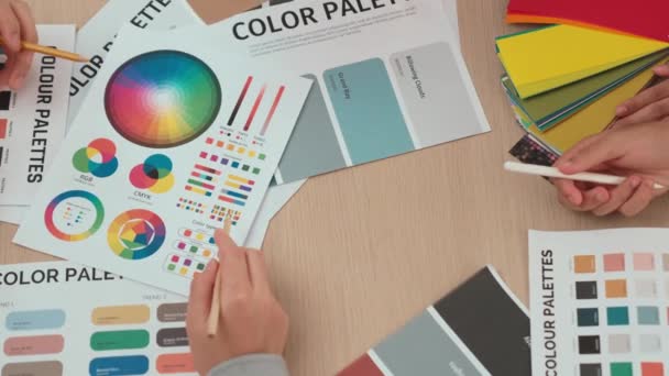 在两位设计师为平面设计工作选择色彩的工作空间表上 或者在设计师创造性的色彩咨询中寻找色彩应用的客户 顶部视图的手工特写 — 图库视频影像