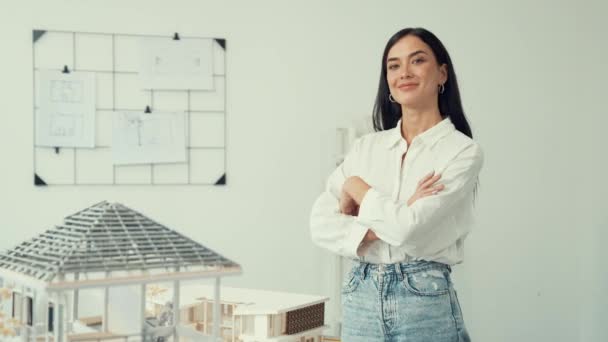 若い美しい美しい建築家エンジニアの肖像画をクロスアームで閉じ ブループリントでホワイトモダンオフィスのハウスモデルに自信を持ってポーズします クリエイティブな生活とデザイン インマキュライト — ストック動画