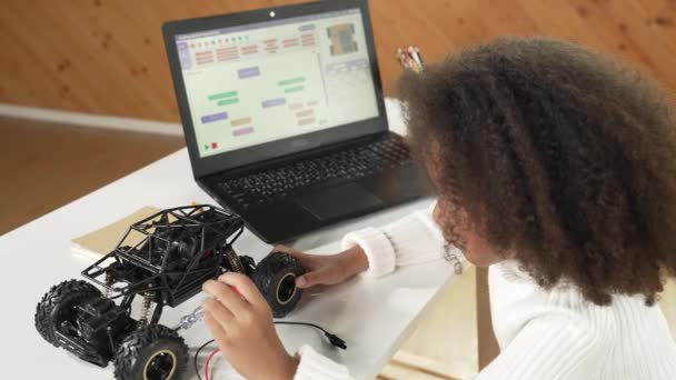 スマートなアフリカの少女は ラップトップスクリーンディスプレイエンジニアリングプロンプトしながら 車のモデルを修理または構築するためにドライバーを使用しています プログラミングとプログラミングシステムを書いている間 ロボット車で働く子供 エラー — ストック動画
