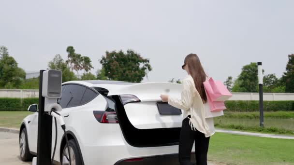 慢动作的女人用购物袋从停车场的充电站给电动车充电 在城市旅游生活方式中 现代女性使用环保电动汽车购物 — 图库视频影像