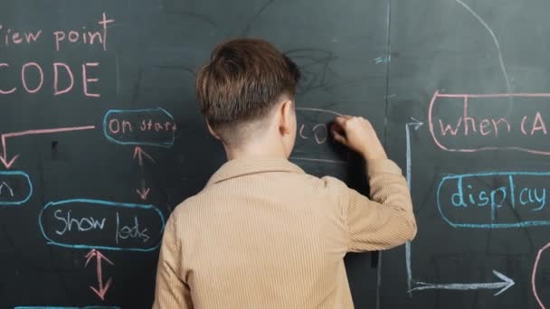 聪明的男孩在黑板上写着工程技术提示 转身对着镜头挥手 用Stem中的编码和编程系统来吸引快乐的学生计划一个项目 穿上衣服Erudition — 图库视频影像