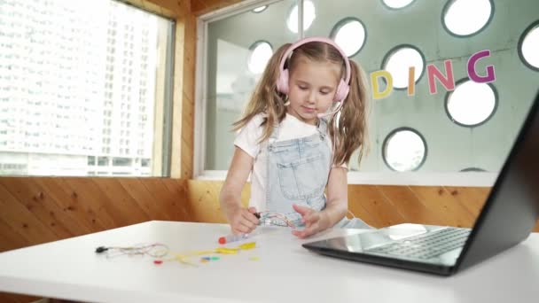 Ładna Dziewczyna Nosi Słuchawki Podczas Badania Sprzętu Elektronicznego Dziecko Robi — Wideo stockowe