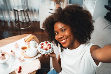 Genç ve güzel Afrikalı blogcu akıllı telefondaki selfie ile konsept özel mutfak konseptinde kek sunuyor. Favori tatlı fırın yemeğiyle sosyal medyanın yaratılması. Tatlandırıcı.
